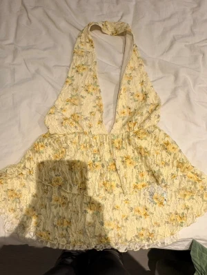 Blommig halterneck linnetopp - Supersöt ljusgul halterneck linnetopp med blommigt mönster i gult och grönt. Toppen har djup v-ringning och är ärmlös, med spetsdetaljer och lätt volang nedtill. Den är endast testad och va för liten för mig därav säljs den!