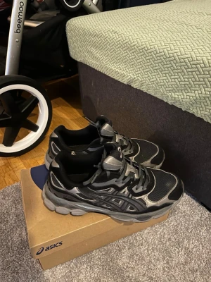 Svarta och grå Asics sneakers - Snygga sneakers från Asics i svart och grått med mesh- och syntetpaneler. Skorna har en chunky sula och klassisk Asics-logga på sidan. Perfekta för dig som gillar sportig och trendig stil.
