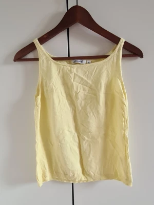 Ljusgul linnetopp från Emily - Ljusgul linnetopp från Emily med smala axelband och enkel, rak passform. Toppen är ärmlös och gjord i mjuk bomull, perfekt för varma dagar. Den har en klassisk design utan mönster eller extra detaljer.