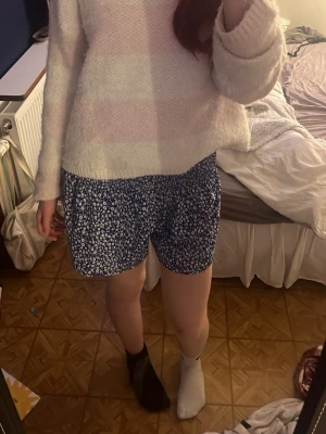 Blå blommiga shorts st 36 - Säljer ett par blå shorts med vitt blommönster och lös passform. Shortsen liknar en kjol men är ett par shorts. Shortsen är perfekta för varma dagar då den är väldigt luftig. De är även lite stretchiga 