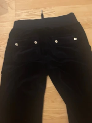 Mörkblå juicy byxor - Säljer ett par svarta mjukisbyxor i mjuk velour med raka ben och bred resår i midjan. Byxorna har snörning framtill och två bakfickor med silvriga knappar. Perfekta för chill dagar eller när du vill vara extra bekväm.