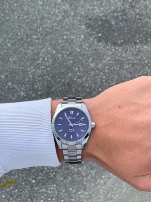 Blå Doventi klocka - Snygg klocka från Ddonasi med blå urtavla och datumvisning. Klockan har ett klassiskt silverfärgat metallarmband och stilrena indexmarkeringar. Perfekt accessoar för dig som gillar en clean och modern look.