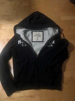 Hollister Hoodie Vintage - Tja! Säljer denna vintage Hollister hoodien med päls på insidan. Hoodien säljs inte längre i butik och är därför väldigt eftertraktad. Priset är ej ristat i sten. Hör av er vid minsta frågor eller funderingar!