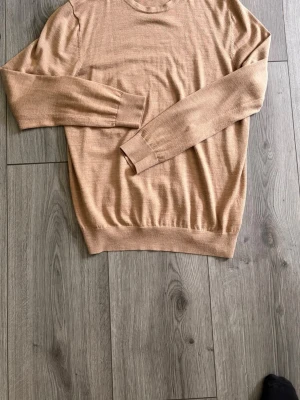 Beige merinoulltröja från H&M - Stickad beige tröja från H&M i merinoullblandning. Klassisk rund hals, långa ärmar och ribbade muddar vid ärmslut och nederkant. Enkel och stilren modell som passar perfekt till lager på lager under höst och vinter.