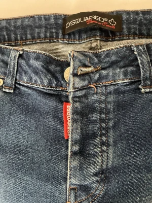 Blå slitna jeans från Dsquared2 - Säljer ett par blå jeans från Dsquared2 med slitningar och trasiga detaljer på benen. Klassisk femficksmodell med röd logotyp-tag vid gylfen och kontrastsömmar. Jeansen har en trendig, avslappnad look och är tillverkade i denim.