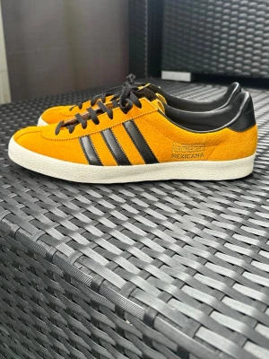 Adidas Mexicana orange sneakers - Snygga Adidas Mexicana sneakers i orange mocka med svarta läderdetaljer och klassiska tre ränder på sidan. Skorna har svarta skosnören och vit sula. Perfekta för dig som gillar retrostil och vill sticka ut med färg.