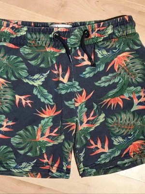 Shorts strl 98/104 kortbyxor med blommor, från Skill - 100% bomull  Har fickor Lite blekare än nya, tycker mig se en liten fettfläck på ett ställe.