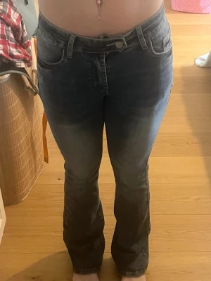 Bootcut jeans i tvättad blå denim - Säljer ett par bootcut jeans i tvättad blå denim med klassiska fem fickor och normalhög midja. Jeansen har en lätt utsvängd passform nedtill och snygga slitningar för en avslappnad look. Perfekta till sneakers eller boots.