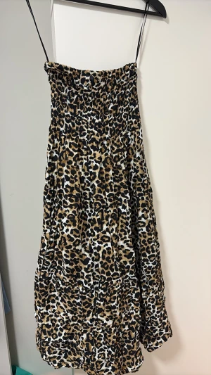 Leopardmönstrad kort klänning - Säljer en snygg kort klänning med leopardmönster och tunna axelband. Klänningen har smock upptill för en bekväm passform och ett luftigt fall. Perfekt för dig som vill sticka ut med ett djurmönster. Materialet känns lätt och passar bra till varma dagar.