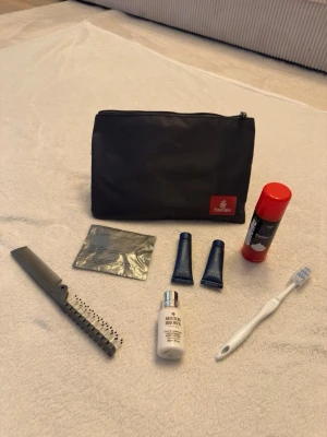 Necessär från Emirates med tillbehör - Snygg svart necessär från Emirates med dragkedja och röd logga. Innehåller tandborste, kam, rakskum, lotion från Molton Brown, ansiktskräm, läppbalsam och våtservett. Perfekt för resan och enkel att ta med sig. Allt på bilden ingår. Allt är såklart oanvänt
