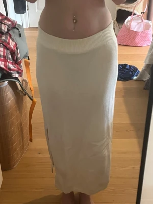 Vit stickad långkjol med slits - Vit långkjol i stickat material med ribbad midja och slits på sidan. Kjolen har en enkel och stilren design som passar perfekt till många olika looks. Mjuk och bekväm passform. Använd mycket men inga tecken på användning. 