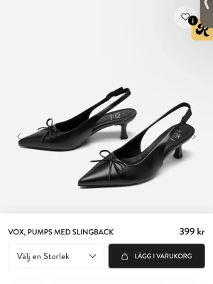 Svarta slingback pumps från VOX - Stilrena svarta pumps från VOX med elegant slingback och spetsig tå. Skorna har en låg klack och en söt rosett framtill. Tillverkade i ett slätt material som ger en klassisk look. Perfekta för dig som gillar tidlös och chic stil.