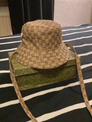 GG Beige bucket hat  - Säljer en beige bucket hat med gg mönster. Lådan ingår inköpet. Pris kan diskuteras vid snabb affär