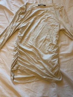 Beige långärmad topp med rynk - Trendig beige långärmad topp med rynkade detaljer längs  sidorna. Toppen har en smal passform och är tillverkad i mjukt bomullsmaterial. Perfekt att styla med jeans eller kjol för en snygg look.