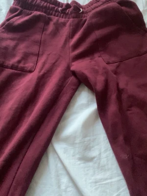 Vinröda bootcut,low waist mjukisbyxor  - Mysiga vinröda mjukisbyxor med resår och dragsko i midjan. Byxorna har två stora fickor framtill och en bakficka. Perfekta för chill eller häng. Tillverkade i mjukt tyg för extra komfort.