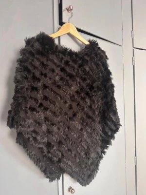 Svart pälsponcho från MacLauren  - Snygg svart poncho i mjuk päls med struktur. Ponchon har en V-formad nederkant och ger en lyxig känsla. Perfekt för att höja din outfit med ett trendigt lager. Passar dig som gillar statement-plagg och vill ha något extra. Från Mac Lauren i storlek onesize men passar S/M.