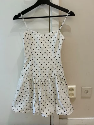 Bershka trendig Vit prickig kort klänning - Söt vit klänning med svarta prickar och tunna axelband. Klänningen har en kort, utställd kjol och smickrande passform. Perfekt för varma dagar och somriga tillfällen. Materialet känns lätt och luftigt.