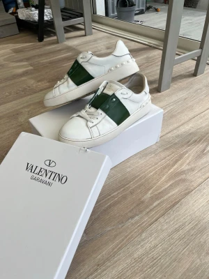 Valentino Garavani vita sneakers - Snygga vita sneakers från Valentino Garavani med gröna detaljer. Skorna finns i storlek 43 och är i prima skick. Hör av dig vid minsta fråga!! Priset är ej hugget i sten!!
