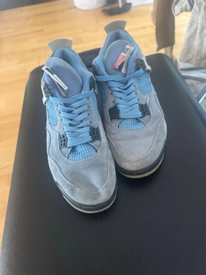 Jordan 4 University Blue sneakers + box - Snygga Jordan 4 University Blue sneakers i ljusblå mocka med meshdetaljer och svarta samt vita inslag. Skorna har klassisk siluett, blå skosnören och specklad sula. Perfekta för dig som vill sticka ut med en ikonisk modell.