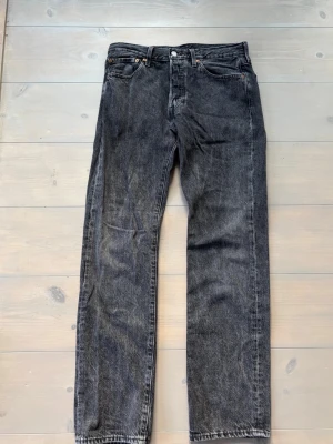 Svarta Levi's 501 jeans raka ben - Klassiska svarta Levi's 501 jeans med raka ben och fem fickor. Jeansen har knappgylf och är tillverkade i slitstark denim. Snygg tvättad svart färg som ger en vintagekänsla. Perfekta för en avslappnad och tidlös stil.