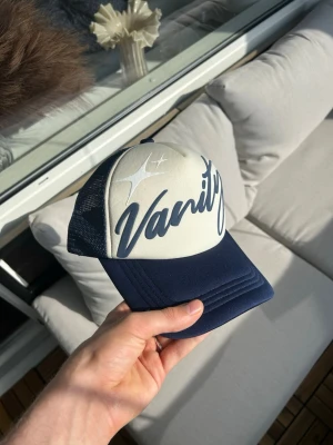 vanitywrld trucker keps - Navy och kräm vit trucker keps, puffprint logga på framsidan med broderad text på sidan