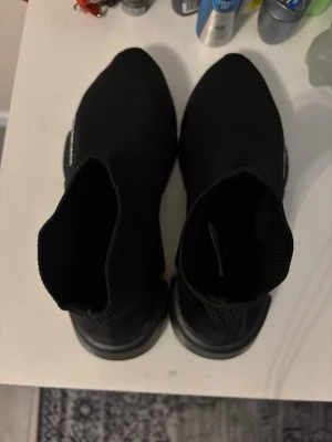Svarta skor - Säljer ett par svarta sneakets med stickad ovandel och chunky sula. Skorna har en strumpliknande passform och loga på sidan. Perfekta för dig som gillar streetwear och vill ha något trendigt och bekvämt.