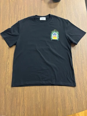 Svart Casablanca t-shirt - Casablanca t-shirt i svart med färgglatt tryck fram och stort grafiskt tryck på ryggen med texten 'Avenida Casablanca'. Start priset 500 kr. 