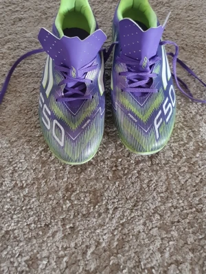 Lila Adidas F50 fotbollsskor - Säljer ett par lila Adidas F50 fotbollsskor med gröna och vita detaljer. Skorna har snörning, låg profil och är tillverkade i syntetmaterial med en innersula i limegrönt tyg. Perfekta för dig som vill sticka ut på planen! Har använt dom några gånger under vintern men i väldigt bra skick. Pris kan sänkas vid en villig affär