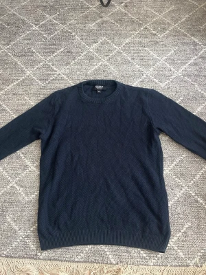 Mörkblå stickad tröja Pull&Bear - Mörkblå stickad tröja från Pull&Bear med rund halsringning och ribbade muddar vid ärmslut och nederkant. Tröjan har en enkel, klassisk design och är tillverkad i ett mjukt stickat material som passar perfekt till lager på lager.