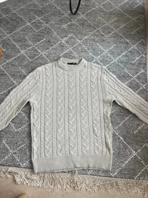 Beige kabelstickad tröja  - Säljer en beige kabelstickad tröja från 157 med rund halsringning och ribbade muddar. Tröjan har ett klassiskt flätmönster och är perfekt för dig som gillar en stilren och mysig look. Passar till allt och är superenkel att matcha.