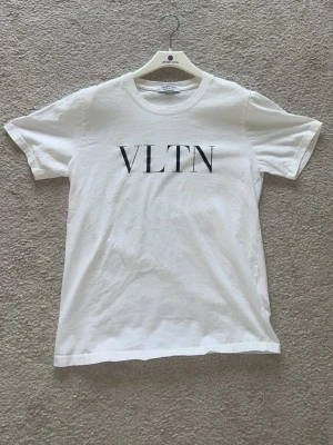  Valentino t-shirt M passar S - Snygg vit t-shirt från Valentino med VLTN-tryck framtill. Klassisk rund halsringning och korta ärmar. Tillverkad i mjuk bomull för en skön känsla och stilren look. Perfekt för dig som gillar exklusiva och minimalistiska plagg.
