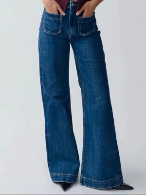 Blåa vida jeans med stora fickor - Säljer ett par blåa jeans med hög midja och vida ben. Jeansen har stora fyrkantiga framfickor och klassisk jeanssöm. Perfekta för dig som gillar en avslappnad och trendig look. Materialet är kraftig denim i bomull. från gina i storlek 34🌼