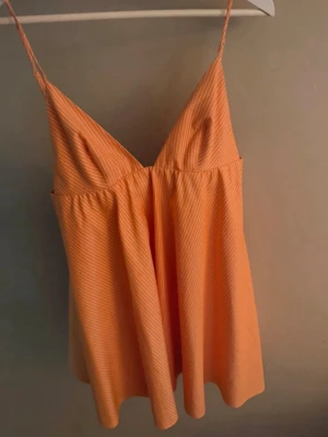  Ny trendig orange klänning från Zara  - Säljer ett persikofärgat klänning med tunna axelband och v-ringning. Klänning har en lös och luftig passform, perfekt för varma nätter. Materialet ser ut att vara mjukt och bekvämt, troligen bomull e. Enkel och stilren design.
