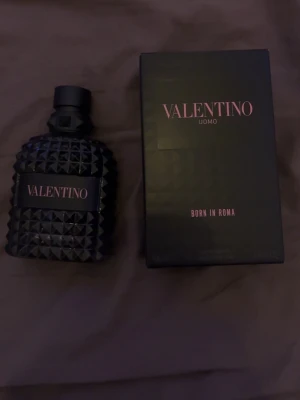 Valentino Uomo Born In Roma parfym - Säljer en Valentino Uomo Born In Roma parfym. Flaskan är svart med nitar och har en lyxig, modern design. Märket står tydligt på flaskan och kartongen. Perfekt för dig som gillar exklusiva dofter och snygg inredningsdetalj på hyllan.