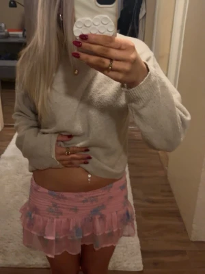 Rosa volangkjol med blommigt mönster - Supersöt kortkjol i rosa med blått blommigt mönster och volangkant. Kjolen har en tight passform och är gjord i ett lätt, tunt material som känns luftigt. Perfekt för dig som vill ha en feminin och trendig look. Kjolen är i storlek M men skulle säga att den passar S bättre. Den är lång men den går att vika ner ganska mycket vilket jag tycker blir snyggare.