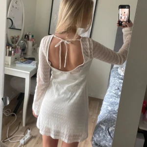 Vit spetsklänning med öppen rygg och knyt - Säljer en söt vit kortklänning med långärmade spetsärmar och vacker öppen rygg med knytband. Klänningen har ett diskret vågigt mönster i spetsen och rund halsringning framtill. Perfekt för sommarens tillfällen och även studenten! ❤️Storleken är större än vad man tror, jag bär normalt sätt S men klänningen passar bra på mig! (Inte mina bilder)