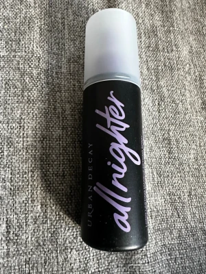 Urban Decay All Nighter Face Mist - Urban Decay All Nighter är en face mist i svart flaska med lila text och matt plastlock. Den håller makeupen fräsch och på plats länge utan att spricka eller flagna. Formulan är lätt och andas, perfekt för att hålla huden sval och fräsch hela dagen.