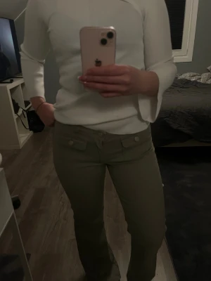 gröna bootcut jeans med fickor - Säljer ett par olivgröna jeans med två framfickor med lock. Jeansen har låg midja och stängs med knapp och dragkedja. Perfekta för en avslappnad och trendig look.