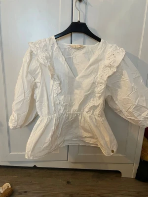 Vit blus med volang från Pernilla Wahlgren - Söt vit blus från Pernilla Wahlgren med volangdetaljer längs v-ringningen och axlarna. Blusen har lång ärm och är tillverkad i ett tunt, lätt tyg som ger en romantisk känsla. Säljs då jag köpt fel storlek och den är förstor. Pris kan diskuteras. Köparen står för frakten. 