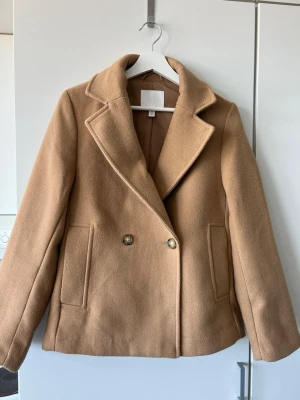 Beige cropped kappa  - Stilren beige kappa från H&M med dubbelknäppning och breda slag. Rocken har två framfickor och är fodrad för extra komfort. Klassisk rak passform som passar perfekt till höst och vinter. Har knappt använt denna. Bär storlek S/36 och XS sitter väldigt fint på. 