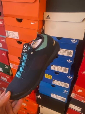 Svarta sneakers från Haglöfs - Snygga svarta sneakers från Haglöfs med turkosa detaljer och matchande turkosa skosnören. Ovandelen är i slitstarkt textilmaterial och skon har en sportig, låg profil. Perfekt för dig som gillar en clean och modern look.