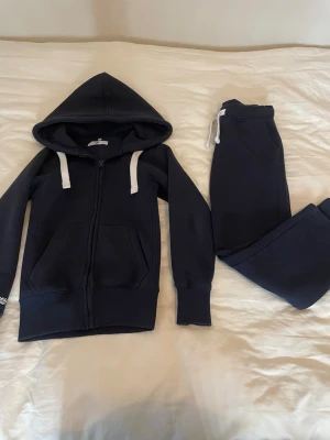 Mörkblått russemerchset i xxs  - Mörkblått loungewear-set med hoodie och matchande byxor från russemerch i storlek xxs. Hoodien har dragkedja, vita snören och fickor framtill samt broderad logga på ärmen. Byxorna har resår i midjan och vita snören. Säljer då de inte kommer till användning. Köpta för 1250kr💕kontakta mig för fler bilder eller om ni endast vill köpa en del!💕är i ett mycket bar skick och är tvättade runt 2 gånger! Pris kan diskuteras!💕