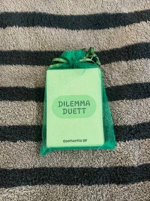 Dilemma Duett kortspel - Dilemma Duett är ett kortspel från Contentia UF där spelare argumenterar kring olika dilemman. Korten är ljusgröna och kommer i en matchande grön tygpåse med snörning. Perfekt för spelkvällar med vänner eller familj! 😝OBS färgerna i bilderna ser lite annurlunda ut pgr av ljuset 🤗