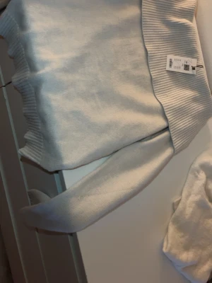 Ljusgrå stickad off shoulder  tröja XS - Ljusgrå stickad tröja med bred ribbad polokrage och ribbade muddar. Tröjan har en avslappnad passform och är tillverkad i mjukt material som passar perfekt för kyliga dagar. Med prislapp