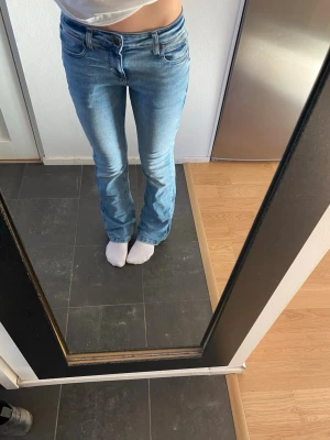 Blå low bootcut jeans från Lee - Säljer ett par klassiska blå jeans från Lee med utsvängda ben och normal passform. Jeansen har Lee-logga på bakfickan och snygga kontrastsömmar. Perfekt för dig som gillar tidlös stil och vill ha ett par jeans som funkar till allt.