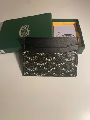 Svart kortfodral från Go4yard - Snyggt svart kortfodral från Go4yard med klassiskt mönster i vitt och grått. Tillverkat i tåligt canvasmaterial med läderdetaljer och flera fack för kort. Perfekt för dig som vill ha en stilren och exklusiv accessoar i fickan.