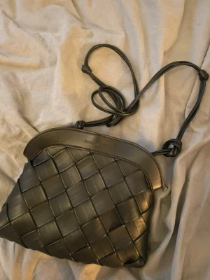  Ny  slutsåld Svart flätad handväska från Carin Wester  - Snygg svart handväska från CALVIN KLEIN i flätad läderimitation. Väskan har justerbar axelrem med knutdetaljer och dragkedja upptill. Insidan har ett praktiskt innerfack med logotyp. Perfekt för dig som gillar stilrena accessoarer.