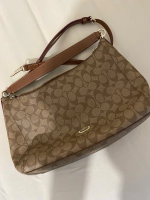 Brun Coach väska  - Helt ny brun handväska från Coach med klassiskt monogrammönster. Perfekt för dig som gillar stilrena accessoarer med lyxig känsla. 