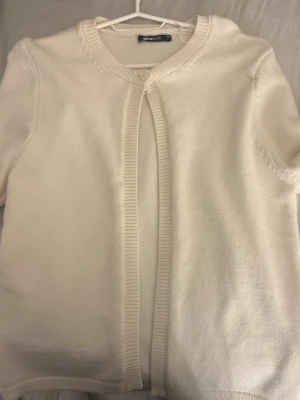 Vit kofta från Esmara - Stilren vit kofta från Gina Tricot med rund halsringning och knapp högst upp. Koftan har långa ärmar och ribbade kanter. Perfekt att slänga över en topp för en enkel och clean look.