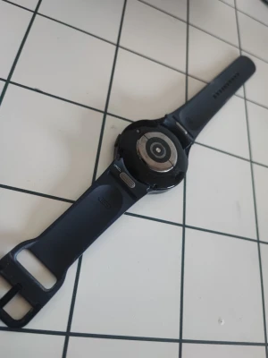 Galaxy watch 6, 44mm skärm + laddaren. - Snygg svart smartklocka från Samsung med rund urtavla och silikonarmband. Klockan har en stilren design och metall på baksidan för pulsmätning. Perfekt för dig som vill ha koll på notiser och hälsa direkt på handleden.